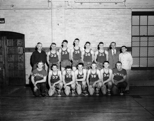 Group portrait of the uniformed Sun Prairie High School boys' basketball team in the gym, along with coaches and team managers.