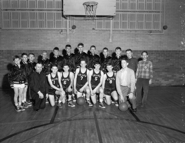 Group portrait of the Blessed Sacrament Grade School basketball team, champions of the Parochial League for 1951 with their principal, Father Schneider, at left front row, and their manager, Jim Huber, at right, front row.