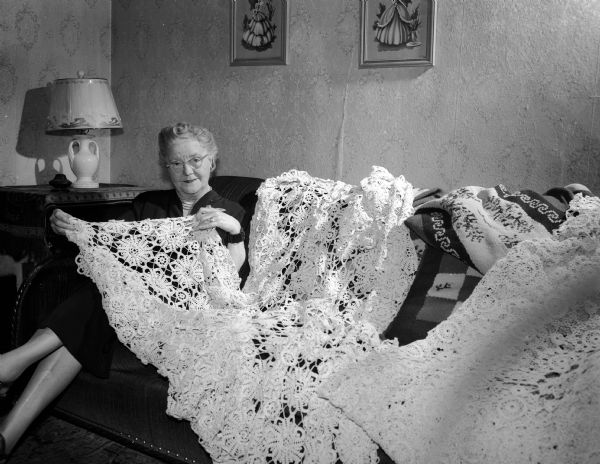 Mrs. Mary Cashel is sitting on a sofa with a crocheted bedspread she made. It will be displayed at the Madison Catholic Women's Club hobby show.