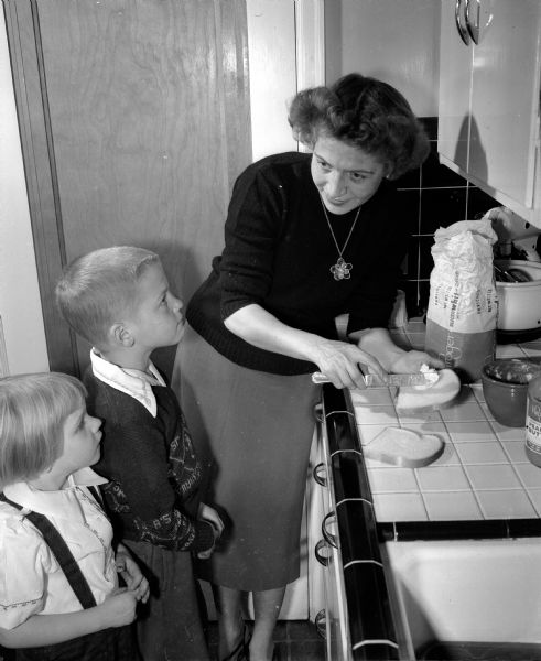 Mrs. Myrtle Cadwell, a retired nurse, butters a piece of bread as two of her three children, Kristi and Carlton, look on. As a graduate nurse she could be called on for duty in case of an emergency.