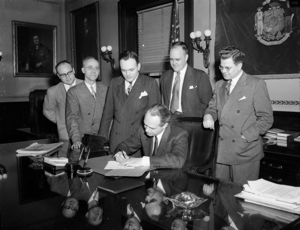 Governor Walter J. Kohler, Jr. signs a bill that would liberalize state housing loans to veterans. The legislators grouped around him in the Governor's office include, (left to right): Theodore Jones (R-Lake Mills); Martin Howard (R-Milwaukee); Roy Sengstock (R-Marinette); Melvin Laird (R-Marshfield)later a U.S. Congressman and Secretary of Defense, directly behind the governor; and Arthur Lenroot (R-Superior).