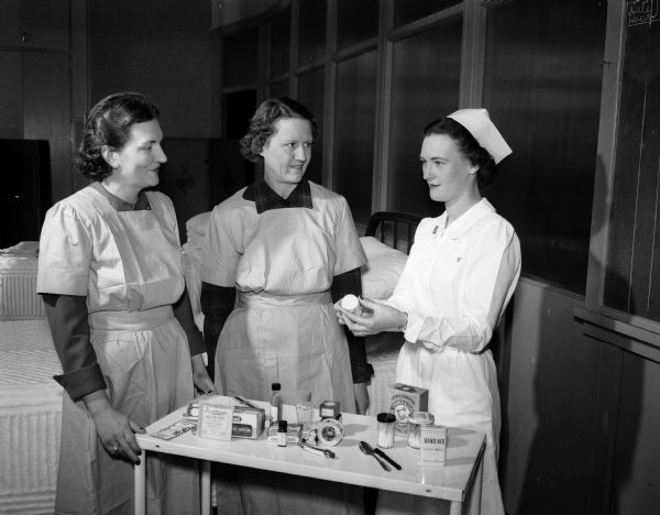 Red Cross nurse instructor, Dorothy Wylde, at right, teaches proper contents of a home medicine chest to Marjorie Hagan, left, and Dorothy Currere, students in the Red Cross home nursing class.