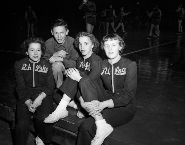The Rib Lake cheerleaders sitting along the sidelines at the University of Wisconsin-Madison Field House during the state boys basketball tournament. From left are: Bethy Schabel, Marty Oman, Mary Ann Hingst, and Caryle Schwoch.