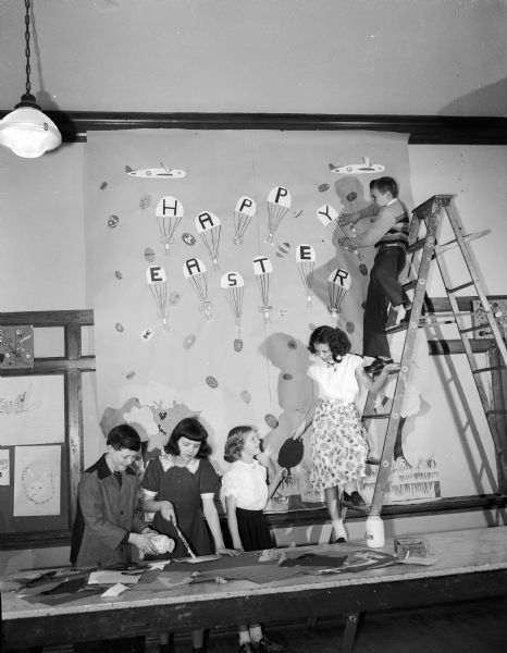 Members of the Emerson Grade School Sketch Club, an after-school group, are pictured preparing a giant "Happy Easter" card for the children at the Orthopedic Hospital under the guidance of their art teacher, Donald J. Reppen. The pupils are, from left to right: David Langhammer, Kathleen Quam, Geraldine Ahlvin, Martha Meier, and on the ladder, Donald Klongland.