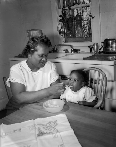 Zelma Stevenson spoon-feeding Jane, a 19-month-old foster child residing at the Stevenson home at 718 West Main Street. Mrs. Stevenson is a member of the foster parents' committee.