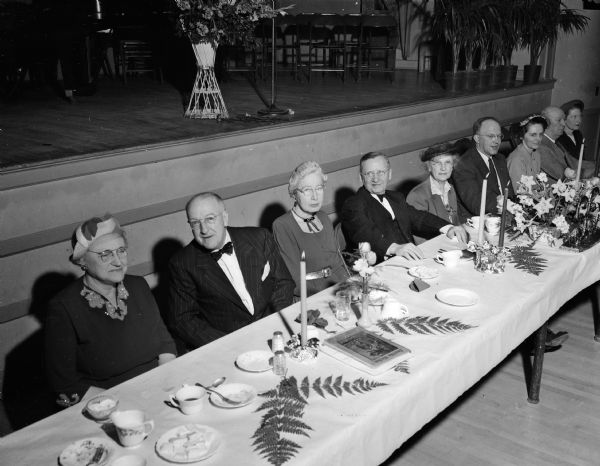 Guests sit at a banquet table during a dinner celebrating the Madison Maennerchor 99th birthday at Turner Hall. Pictured from left to right are: Mrs. Alexius H. (Evalyn) Baas, Mr. Bass, Grace L. Snell, Otto A. W. Niemann, Mrs. Caroline Niemann, County Judge George Kroncke, Jr., Mrs. Jane A. Kronche, Atty. Harry Sauthoff, and Mrs. Lenore D. Sauthoff.