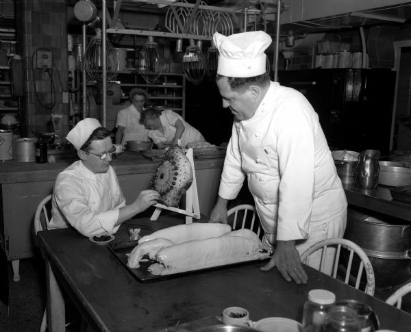 Paul Cleary gets instructions on how to decorate a baked ham from head chef Maurice Comos for the Smorgasbord at the University of Wisconsin Memorial Union. Two salmon are visible on a pan on the table.