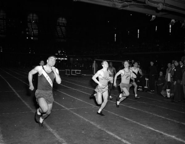 Action shot during West High School's invitational track meet at the University of Wisconsin-Madison Field House. Shown are six competitors racing toward the finish line.