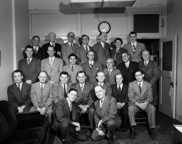An informal portrait, taken at a caucus at city hall, shows Madison's City Council, the city's mayor, and two of its top officials. In the foreground are City Clerk Alfred W. Bareis and City Attorney Harold E. Hanson. Mayor-elect George J. Forster is in the center of the first row. Mrs. Ray A.(Ethel) Brown, second from right in the top row, is the first woman council member in Madison's history.