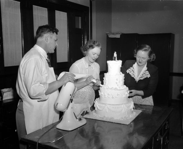 Victor Hammersley, a professional baker and teacher, supervises as Elizabeth Zweifel and Mae Grelle decorate a cake at the Madison Vocational School.