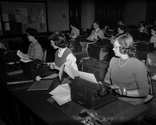 Ferne Stone, Madonna Egan, and Vivian Williams practice typing in the Madison Vocational School commercial department's night school typing class. Eight other students are in the background.