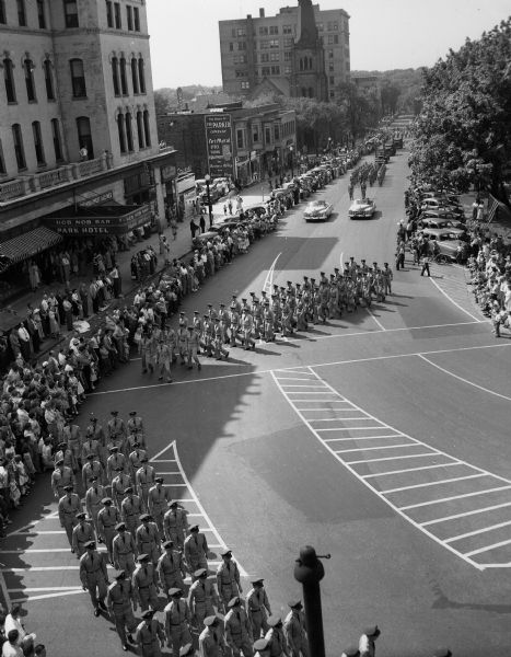 Elevated view of the Armed Forces Day parade, showing servicemen marching on the Capitol Square past the Park Hotel on South Carroll Street.