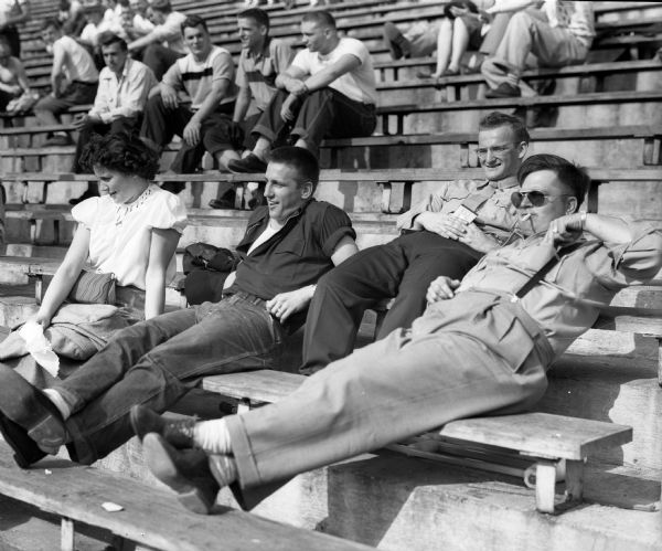 Spectators recline in the stands while watching the University of Wisconsin spring football game. They include, from left: Dorothy Denk and Harland Carl, UW football player, not playing because of knee surgery. The two men to his right are unidentified.