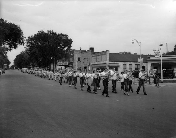 A parade consisting of a band and baseball players is walking down Main Street to celebrate the opening day of Little League baseball in Reedsburg.