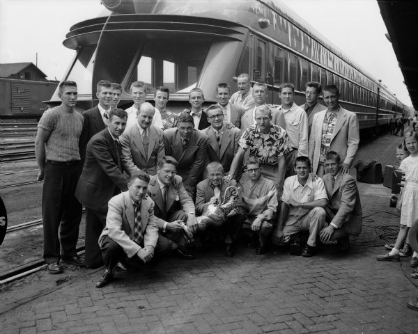 Group portrait of the University of Wisconsin Varsity Crew at West Washington Avenue railroad station. The crew poses before an unusual Milwaukee Road Railroad rear passenger car. The rowing team is shown with their trophy that they won in Marietta, Ohio.