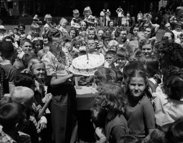 A crowd of children surround a man with a birthday cake while celebrating the first anniversary of Winkie the elephant's arrival at Vilas Zoo.