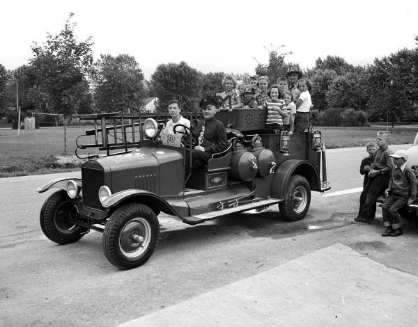 Children riding in a 1923 vintage fire truck at the Shorewood Hills Fourth of July celebration.  Driver of the truck is Dobby Dotson and with him in the pasenger seat is John Dutten.  Riding on the back with the children is Thomas Van Zander, Shorewood Hills village police and fire commissioner. The fire truck was the Middleton fire department's first motorized fire-fighting vehicle.