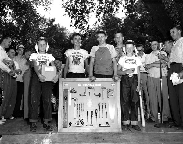 Five of the winners in the Soap Box Derby competition pose with their prizes. Left to right are Billy McFarland, Darlington, winner of the best upholstery award; Jack May, Mineral Point, winner of Shell's $100.00 tool board for best construction; Dick Moon, Richland Center, winner of the best brakes award, an official tennis racquet; Bob Cutting, Richland Center, who won the hard luck award, a Cocker Spaniel puppy; and Mike Welch, Madison, who won the First National Bank award of a $25.00 savings account for sportsmanship.