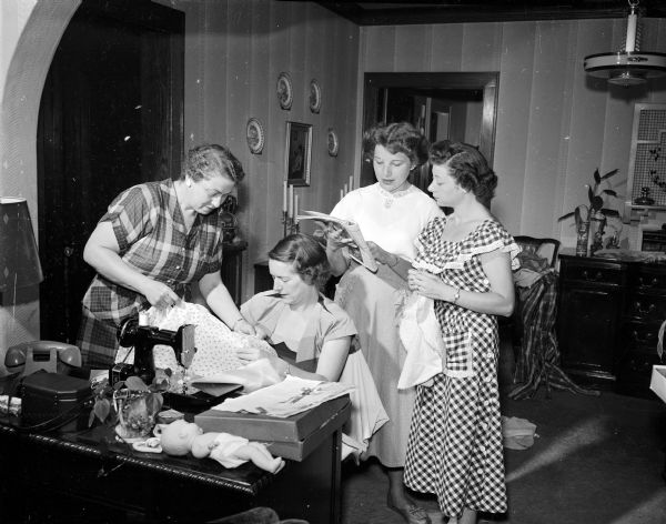 Four members of the Beth Israel Sisterhood gather around a sewing machine while creating items for the upcoming annual Beth Israel bazaar.  Pictured from left to right are: Mrs. Morris (Belle G.) Richman, Mrs. Sam J. (Judith R.) Stein, Mrs. Ben (Roslyn) Kopelberg, and Mrs. Julius (Dorothy K.) Zimmerman.