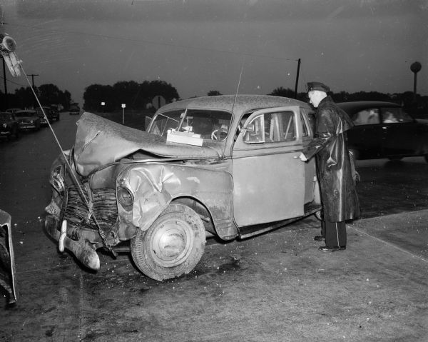Police investigator Boyd Hustad examines the car which a Chicago couple, Mr. and Mrs. Hugh Lee, and two children were riding in when it struck the Runion car broadside at the intersection of Nakoma Road (Hwy 18-151) and the Beltline (Hwy 12,14,18).  Mrs. Harris Runion, St. Louis, Missouri, was killed; her husband and their grandson Thomas Woolsey, Madison, were thrown out of their car.
