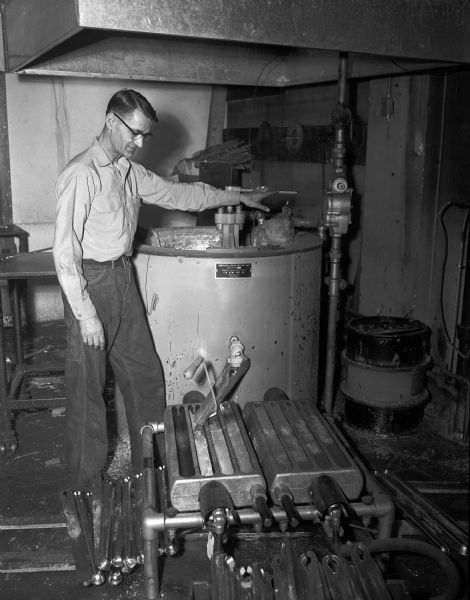 A man operates a natural gas fired kiln used to case metal rods from molten metal (?). Molds are visible at the base of the kiln.