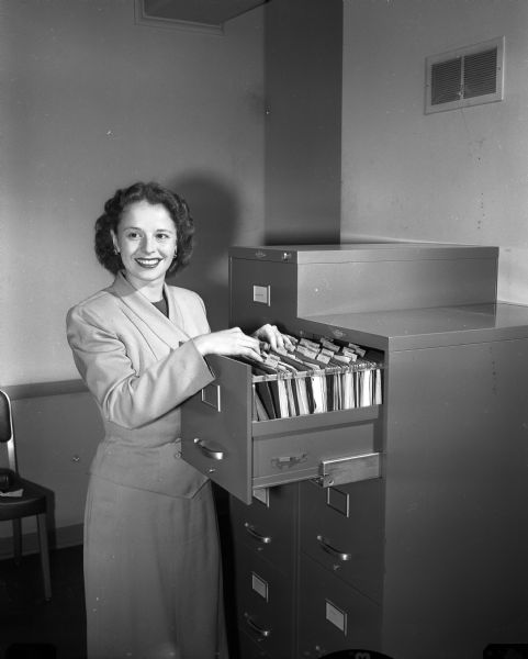 Joyce Bergmann, Waunakee, opens a file drawer in an office. She is the private secretary for Adolph C. Bolz, vice-president and plant manager of Oscar Mayer and Co.
