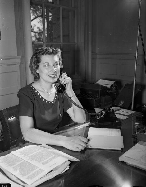 Eleanore Oimoen of 445 West Gilman Street answers a phone call in an office. She is a secretary for Edwin B. Fred, University of Wisconsin president.