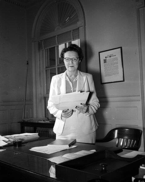 Lola Bradford, of 933 Waban Hill, standing at a desk in an office. She is secretary and administrative assistant for Edwin B. Fred, University of Wisconsin president.