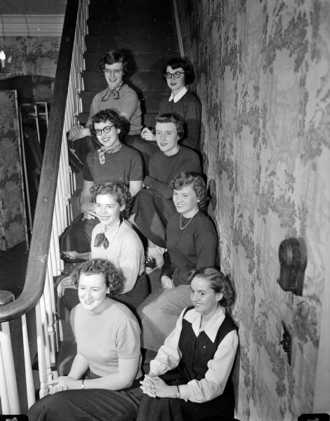 Eight new Madison pledges of the Alpha Gamma Delta sorority at the University of Wisconsin pose for a group portrait on a staircase. On the left, top to bottom, are: Ann Wilson, Nancy Fay, Nancy Kamm, and Patricia Chandler. On the right, top to bottom, are: Becky Marshner, Nancy Moe, Barbara Follett, and Virginia Stamm.