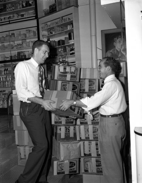 Jack Myers and Roger McHugh, co-managers of the Prescription Pharmacy at 26 South Carroll Street, are shown at their store preparing 50 packages of clothes for Korean children. The taped-shut cardboard boxes have Mautz Paint logos.