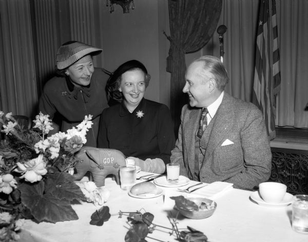 Featured speaker at the Dane Country Women's Republican club luncheon is Suel Arnold, seated at right, chairman of the Milwaukee County GOP and former assistant attorney general. Also shown standing at left is Mrs. E. W. (Constance) Holmquist, vice-chairwoman of the club; and seated, Mrs. W. W. Fox, club president.
