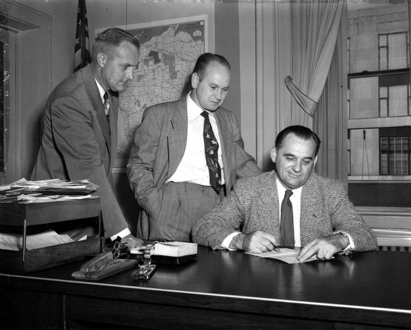 Madison mayor George Forster signs the proclamation to observe Oil Progress Week, while Arnold Wake (center), the general chairman for the observance, and Walter Wildeman, publicity chairman, look on.