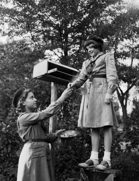 On Girl Scout Sunday, Dane County scouts and their leaders begin the seven service days of Girl Scout week, celebrated nationally to honor Julliette Low, founder of the organization in 1912. Phyllis Rauch, 2723 Van Hise Avenue, at left, and Judy Schmitz, 25127 Norwood Place, ar right, seventh graders of Troop 91 at Blessed Sacrament school, are shown preparing a feeding station for birds as their scouting project.