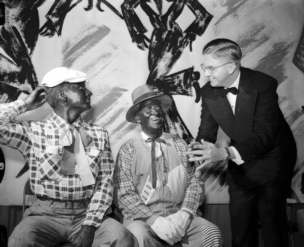 The "Old South" came to life as the Shorewood Hills Community League presented its minstrel show to Shorewood Hills residents and guests. Playing the roles of "end men" (in blackface) are Fritz Carpenter (left) and Dr. J.T. Schawb (right) exchanging jokes with the aid of master of ceremonies, Dr. Robert C. Perkin, (standing far right).