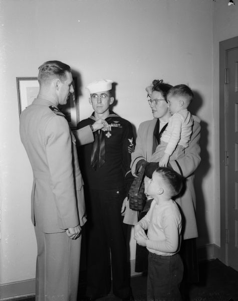 Dale N. Gillings, center, of Middleton and a former naval aviation radioman receives the Distinguished Flying Cross from Commander J.E. McCue of the Madison naval reserve training center. He also received the Air Medal with two gold stars for heroism in action while in combat during the Pacific island campaigns in 1944. On the right are his wife and two of their three sons.