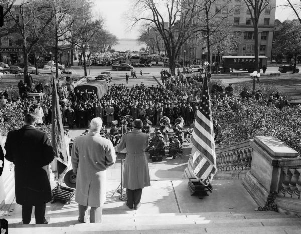 Governor Walter Kohler addresses a group of volunteers assembled at the Wisconsin State Capitol as part of Wisconsin's first civil defense support battalion test in Madison. On the far left  is Carl W. Gabel of Chicago, the regional director of the federal civil defense administration. On his right is General Ralph J. Olson, state director of civil defense.