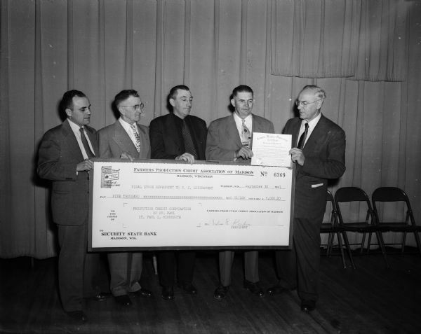 Dane County area directors of the Dane County Area Production Credit Association present an enlarged $5,000 check as final payment of a $120,000 loan to George Sussens, district president, St. Paul, Minnesota. Credit Association area officers, standing left to right are, Glenn Gerhardt, Madison,  E.F. Ryan, Lodi, Adam Pancake, Whitewater and Julius Drebs.
