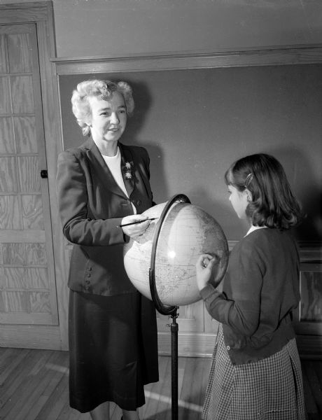 Portrait of Dudgeon School fifth grade teacher Mable Day with one of her pupils reviewing a globe of the world.
