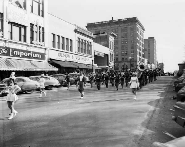The Cambridge High School marching band goes down North Pinckney Street during the Scrap Metal Parade around the Capitol Square. Shown in the background are the Emporium and Olson and Verhusen stores. Proceeds from sale of the metal went towards a movie projector for Cambridge High School.