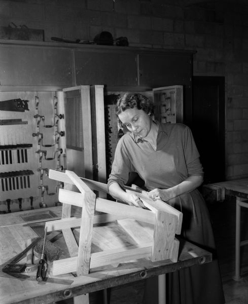 Constructive Workshops for Older Adults, created by the Vocational School, offers many leisure time activities for newly retired men and women. Margaret Langhear is pictured making a saw bench in the woodworking shop,