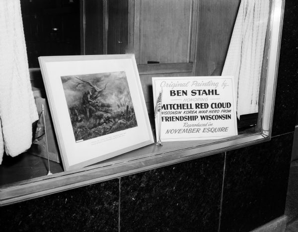 Photograph of a framed painting by Ben Stahl titled "Corporal Red Cloud's Last Stand." It was painted especially for "Esquire" magazine and honored Mitchell Red Cloud who was a Wisconsin Korea war hero from Friendship.