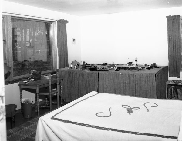 Interior view of the David & Florence Bade residence at 5701 Winnequah Road in Frost Woods, Monona. The photograph shows Jimmy's (age 8) bedroom, including a big table with electric trains on it. His draperies and the trim on the white bedspread are bright red chenille.
