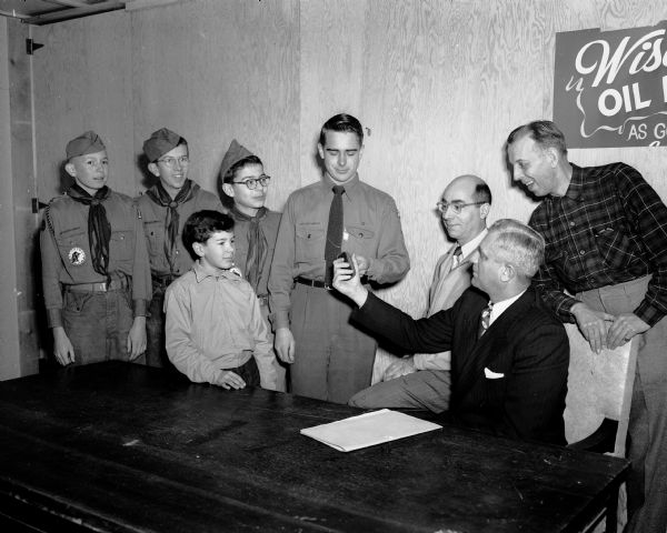 Freeman Fox (seated at right) vice-president of the West Side Business Men's Association (WSBMA) turns over the keys to the clubhouse on Odana Road to members of Boy Scout Troop #18.  Tenderfoot Kenny Kelm is pictured at the left front. Other troop members are, left to right,Dick Green, first class scout; Francis Green, star scout; Jimmy Deuel, second class; Scoutmaster Bill Beduhn, receiving the keys; Pete Deuel, assistant scout master and Win Guenther, troop committee chairman.