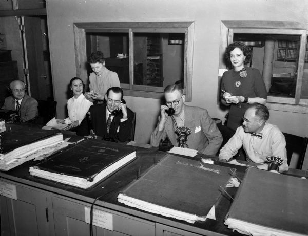 Portrait of part of the crew of fund raisers who helped get pledges from radio listeners in a marathon jamboree on WISC and WISC-FM to benefit the <i>Wisconsin State Journal's</i> Empty Stocking Club. Seated left to right: W.M. "Dixie" Greeley, the station's chief engineer; Mrs. Esther Sager, WISC; Ralph O'Connor, station manager; Roundy Coughlin, State Journal sports columist, and Bill Doudna, State Journal radio editor. Standing left to right: volunteer Mrs. F.R. (Alice) Shores and Doris Ardeit, WISC.