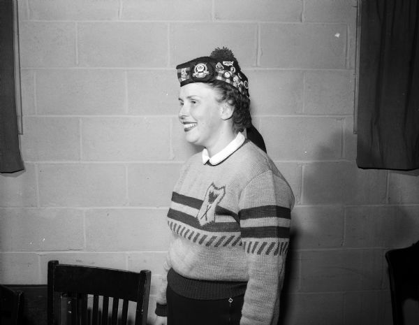 Marion Leifer, a member of the Madison Toories — a women's curling group, is shown wearing a team Scotch hat decorated with pins displaying her curling experiences.