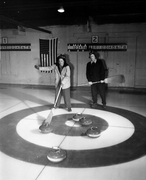 Marion Cottrell, left, and Mildred Solheim, right, holding brooms on the curling rink. The women are "skips" for opposing teams of the Madison Toories, a women's curling group.