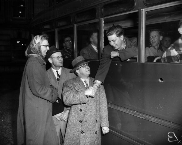 Pvt. Tom Voigt, Ixonia (at right), one of forty-seven "Operation Badger" Air Force recruits sworn in at Madison, shakes hands with his father, Ray Voigt (right), as the air force bus pulls away from the Wisconsin State Capitol steps on its way to Truax Field, and from there to San Antonio, Texas. Also standing beside Mr. Voigt are Mr. and Mrs. Lehmann, Watertown, parents of Tom's fiancé, Carol.
