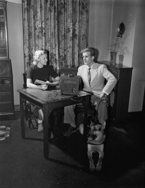 Harriet Kirchhoff, Delta Gamma Sorority member, reading to a blind student, Robert Langford, as part of a University of Wisconsin Student Service project. A dog is sitting under the table at Robert's feet.