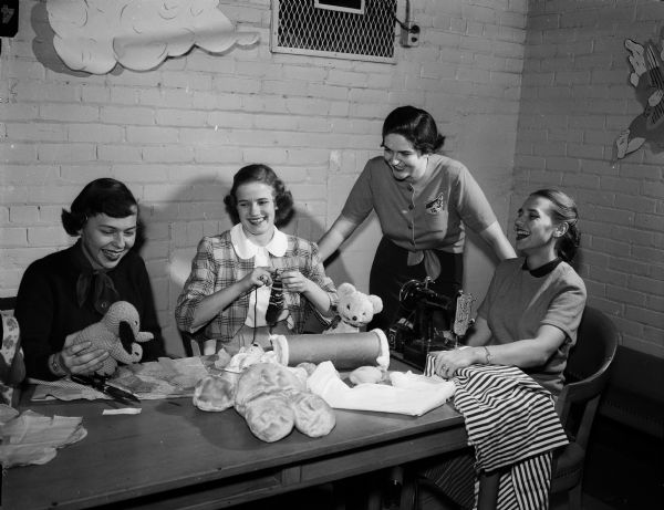 Residents of Elizabeth Waters Dormitory make stuffed toys for Empty Stocking Club and tray favors for patients at Madison General Hospital. Left to right: Nancy Playman, Appleton; Shirley Jevne, Eau Claire; Betty Beaver, Manitowoc; and Murial Puhl, Milwaukee.