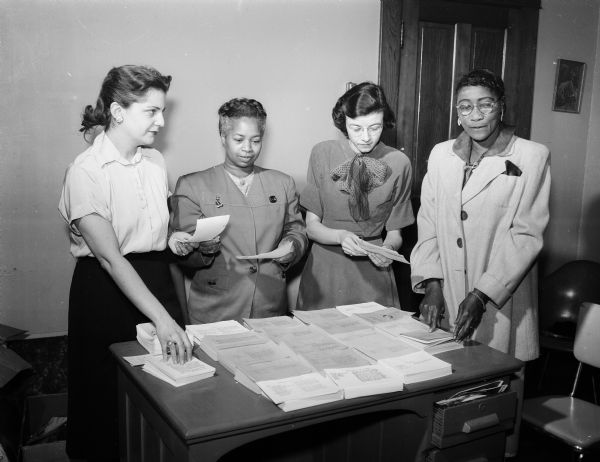 Four members of the Friendship Club stand around a table while assembling a cookbook. Left to right, Mrs. Malcom Gordon, Gertrude Taliaferro, Mrs. William Cook and Ola Jordon. The Friendship Club is an interracial women's club, formed to develop mutual understanding among themselves to answer the problem of segregation-ignorance.